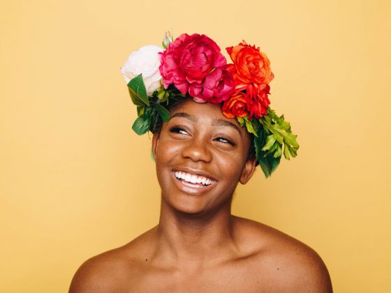 A woman wearing a flower crown in front of a yellow background, smiling.