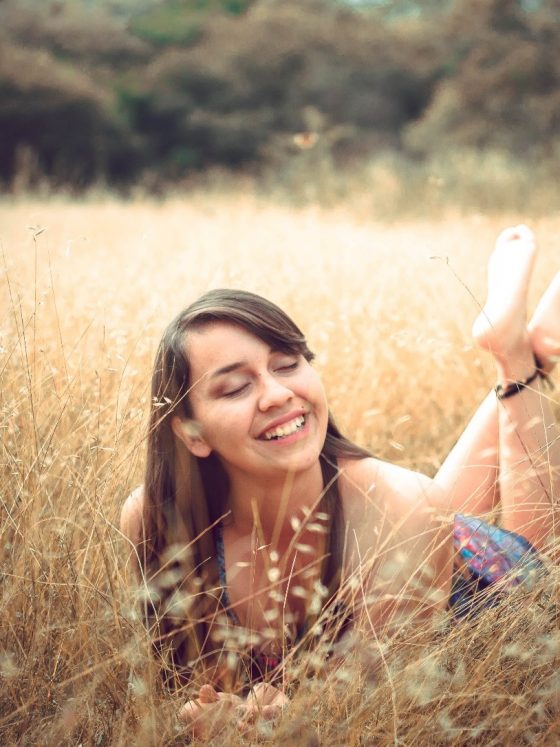 A woman lying barefoot in a grass field, smiling.