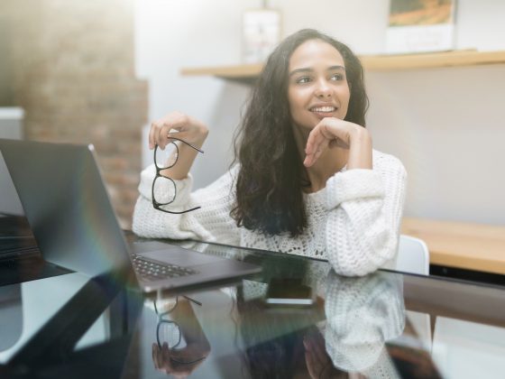 Smiling young woman using laptop thinking about money and finances