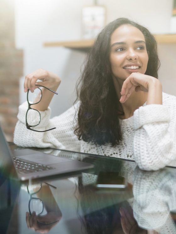 Smiling young woman using laptop thinking about money and finances