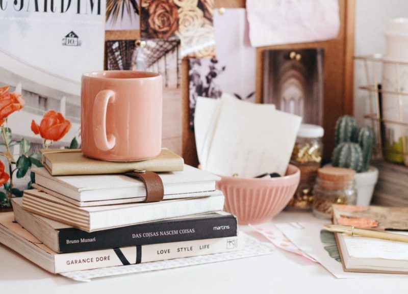 A desk with many pink items on it, including a pink mug, pink bowl, and some pink books.