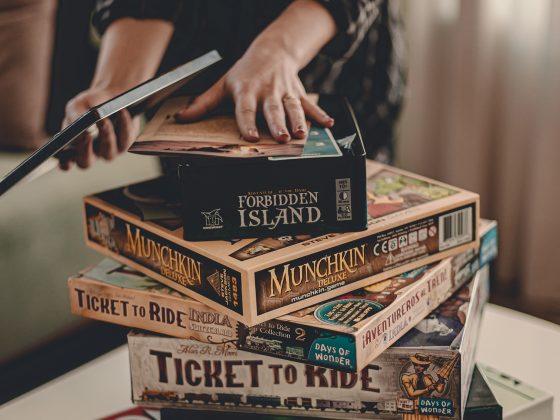 man choosing from collection of board games on top of a table stacked on top of each other